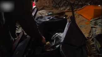 A soldier’s hand searches through a bag containing several items that are not clearly identifiable in the photo.