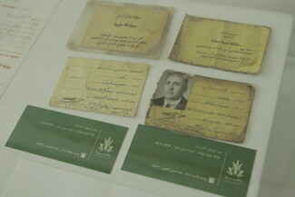 A top-down view of several old, weathered yellow identification documents with Arabic handwriting, one displaying a black-and-white portrait photograph, laid out next to green labels.