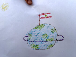 A child's crayon drawing depicting a ringed planet Earth with a Lebanese flag planted on top under a yellow sun.