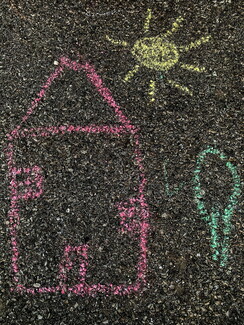 A simple outdoor chalk drawing on dark asphalt showing a house outlined in pink, a sun in yellow, and a key-like symbol in green.