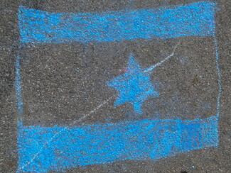 A bright blue chalk drawing on dark asphalt depicting the flag of Israel, featuring a Star of David between two horizontal stripes, with a thin white chalk line drawn diagonally across the star, crossing it out.