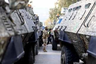 A soldier stands between military vehicles on a street, conveying tension and readiness.