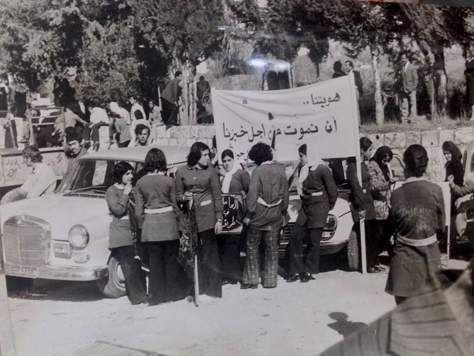 Young women in factory uniforms hold a banner that reads, “our identity is to die for our bread.” Date unknown. Source: Al-Anwar newspaper.     