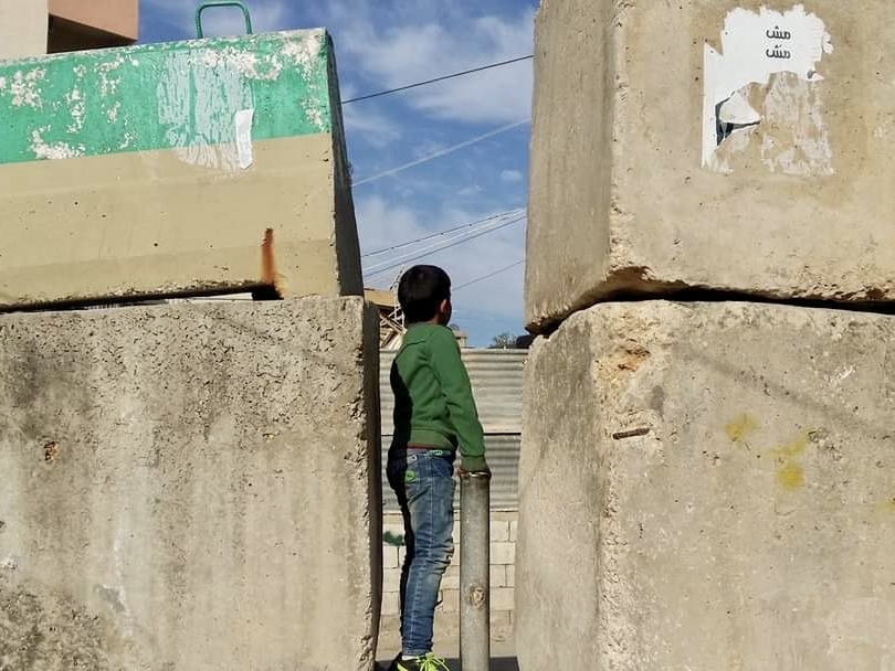 A child stands in a narrow opening between concrete blocks. The Lebanese army limits the passage of cars into a number of Palestinian camps through checkpoints and closes other entrances with concrete walls, leaving only pedestrian pathways. Burj al-Shemali camp, Tyre. January 21, 2017. (Nadia Ahmad/The Public Source)