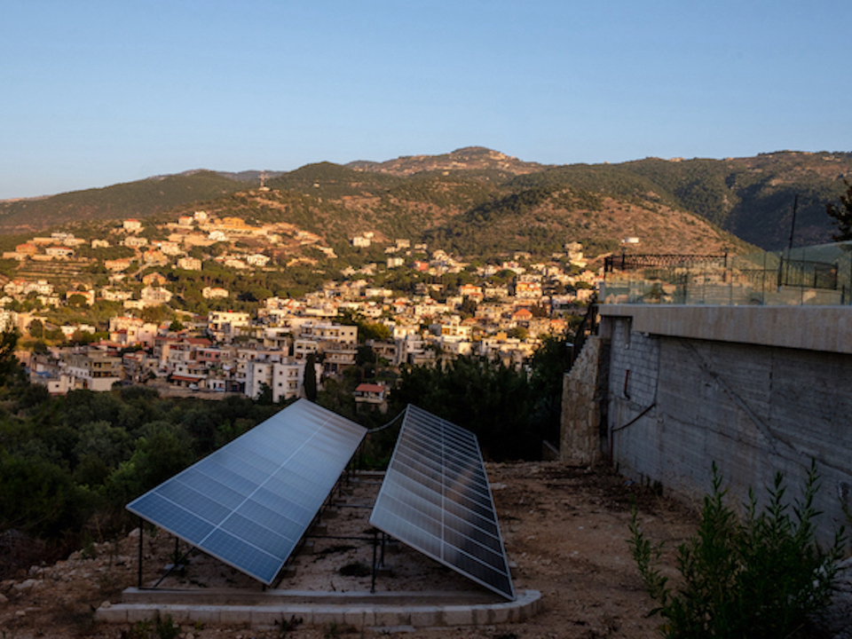 Two rows of solar panels installed on land surrounding villa that oversees a village. 