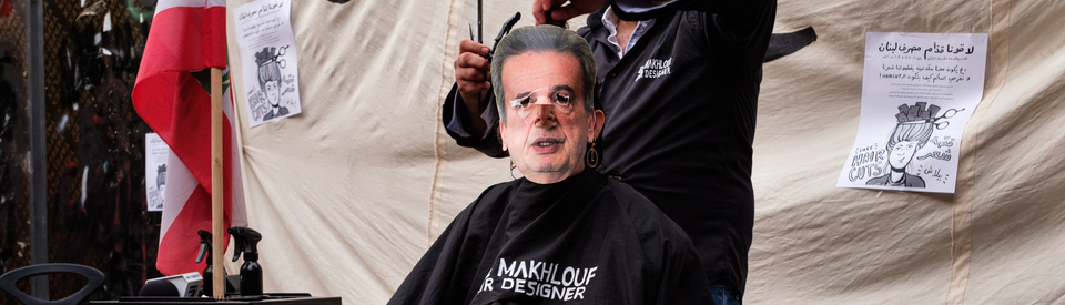 A protester wears a mask depicting central bank governor Riad Salameh’s face while getting a “haircut” in front of the Central Bank.