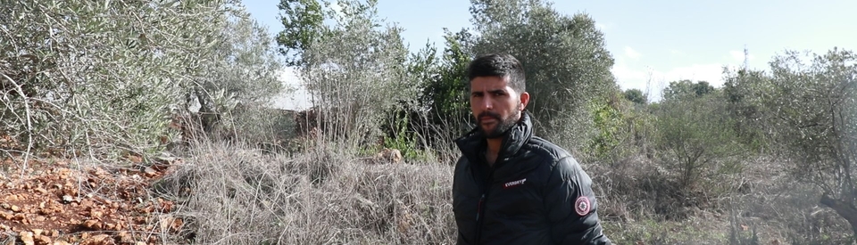 Man wearing black standing in front of his farm in the border town of Dhayra, South Lebanon. He is surrounded by burnt trees and grass impacted by Israel's White Phosphorus attacks. 