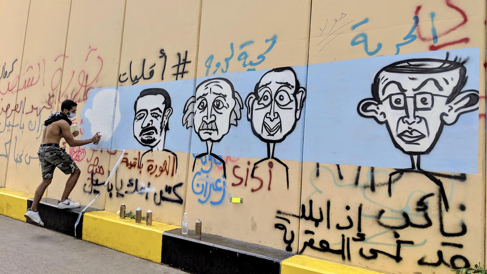 فنان غرافيتي يرسم جدارية لبعض أوليغارشيي لبنان على حائط نُصب قرب ساحة رياض الصلح في وسط بيروت. ٢٤ تشرين الأول ٢٠١٩. (لارا بيطار، مصدر عام)
