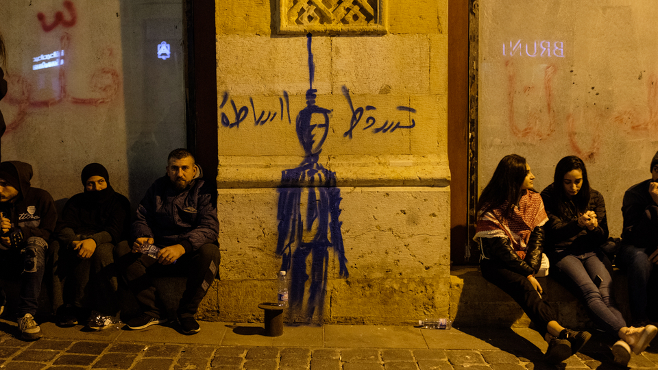 متظاهرون يرتاحون قرب رسم يظهر فيه مشنوقا شخصا يمثّل السلطة. وسط بيروت، لبنان. ١٥ كانون الأول ٢٠١٩. (ريتا قبلان، مصدر عام)