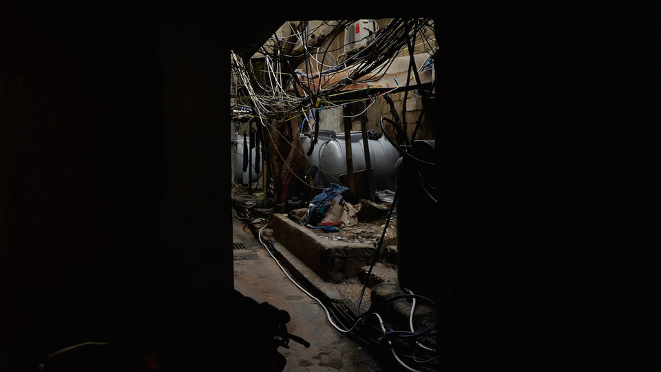 A black background with a rectangular frame showing a network of electrical wires at street level in one of the narrow streets of Mar Elias camp. Mar Elias camp, like all Palestinian camps in Lebanon, suffers from dilapidated infrastructure. Mar Elias camp, Beirut. April 11, 2021. (Mohamad Cheblak/The Public Source)
