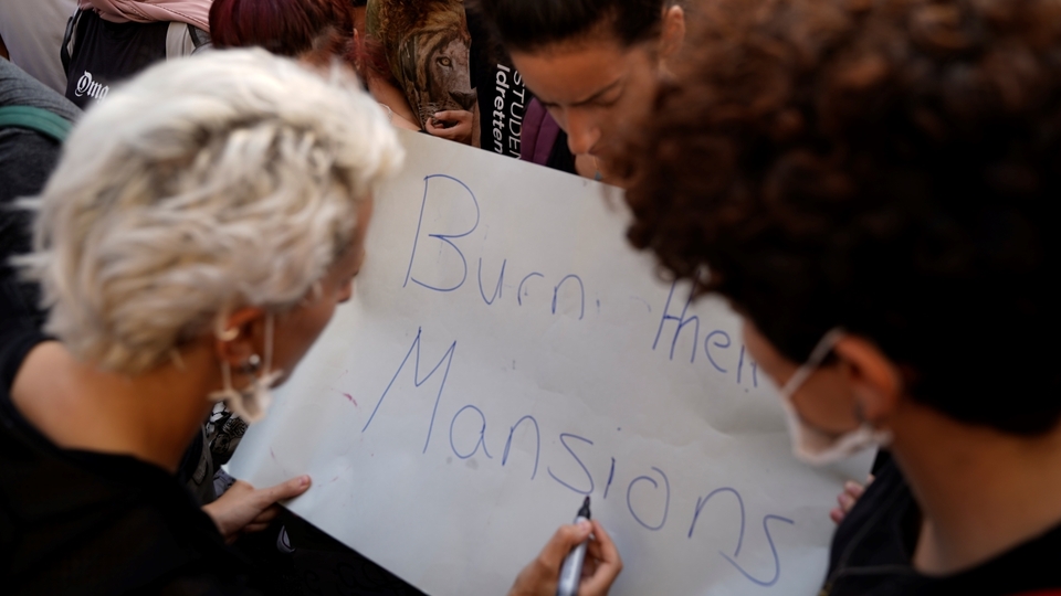 Three protesters hold a sign in Riad al-Solh Square that reads, “burn their mansions." Beirut. Lebanon. October 18, 2019. (Mohamad Cheblak/The Public Source)