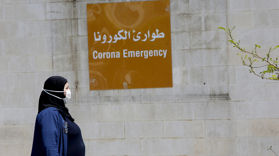 امرأة تمر أمام يافطة "طوارئ الكورونا" معلّقة في مستشفى رفيق الحريري الجامعي. بيروت، لبنان. ١٧ نيسان، ٢٠٢٠. (مروان طحطح، مصدر عام)