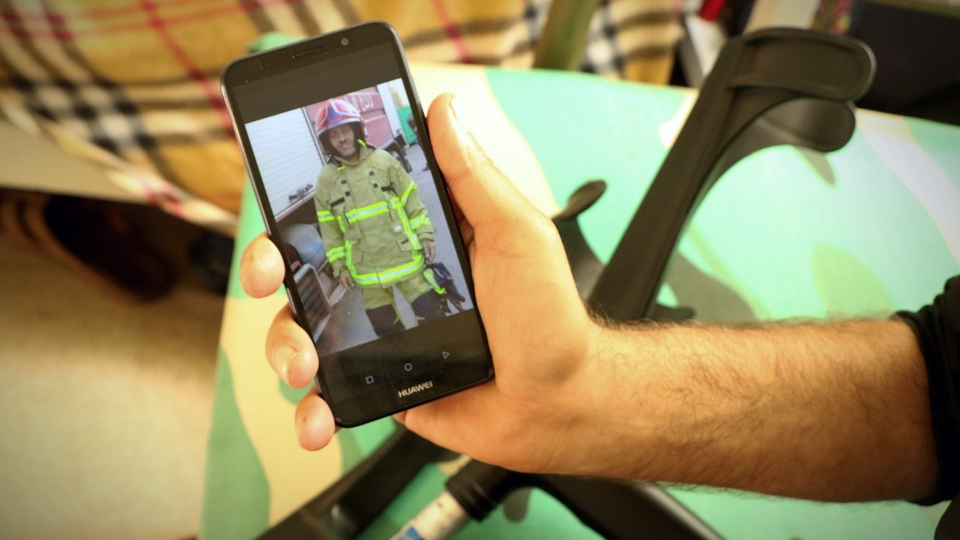 A close-up of Abed’s arm holding his phone displaying a picture of himself in full firefighter gear. In the background, crutches.  