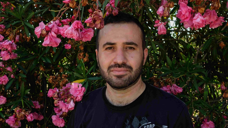 Portrait of Mohammad Ali, dressed in a black T-Shirt, against a flowering pink tree.