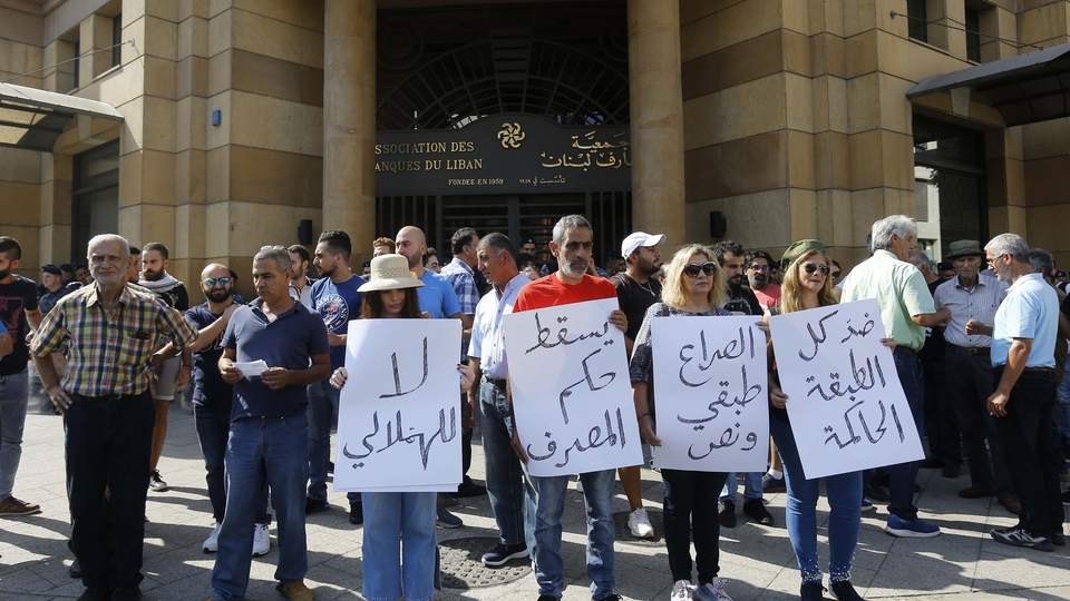 Protesters standing in front of the headquarters of the Association of Banks of Lebanon, carrying signs that read “Down with the rule of the banks.”
