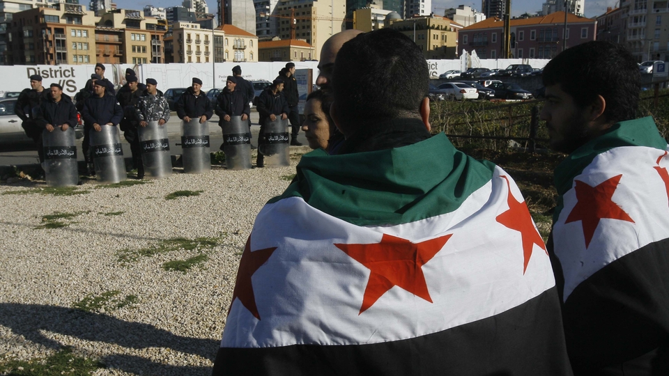 Supporters of the 2011 Syrian uprising, draped in the Syrian opposition flag, gather to commemorate its first anniversary, as members of Lebanon’s Internal Security Forces watch in relaxed shield formation. Martyrs’ Square, Beirut, Lebanon. March 17, 2012. (Marwan Tahtah/The Public Source)
