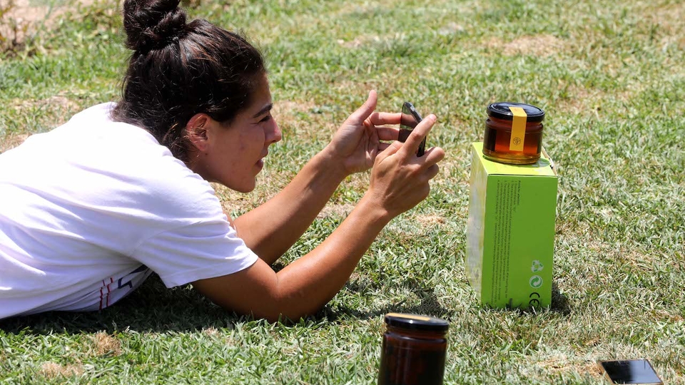 Moné Makkawi lies on the grass to photograph a jar of honey.